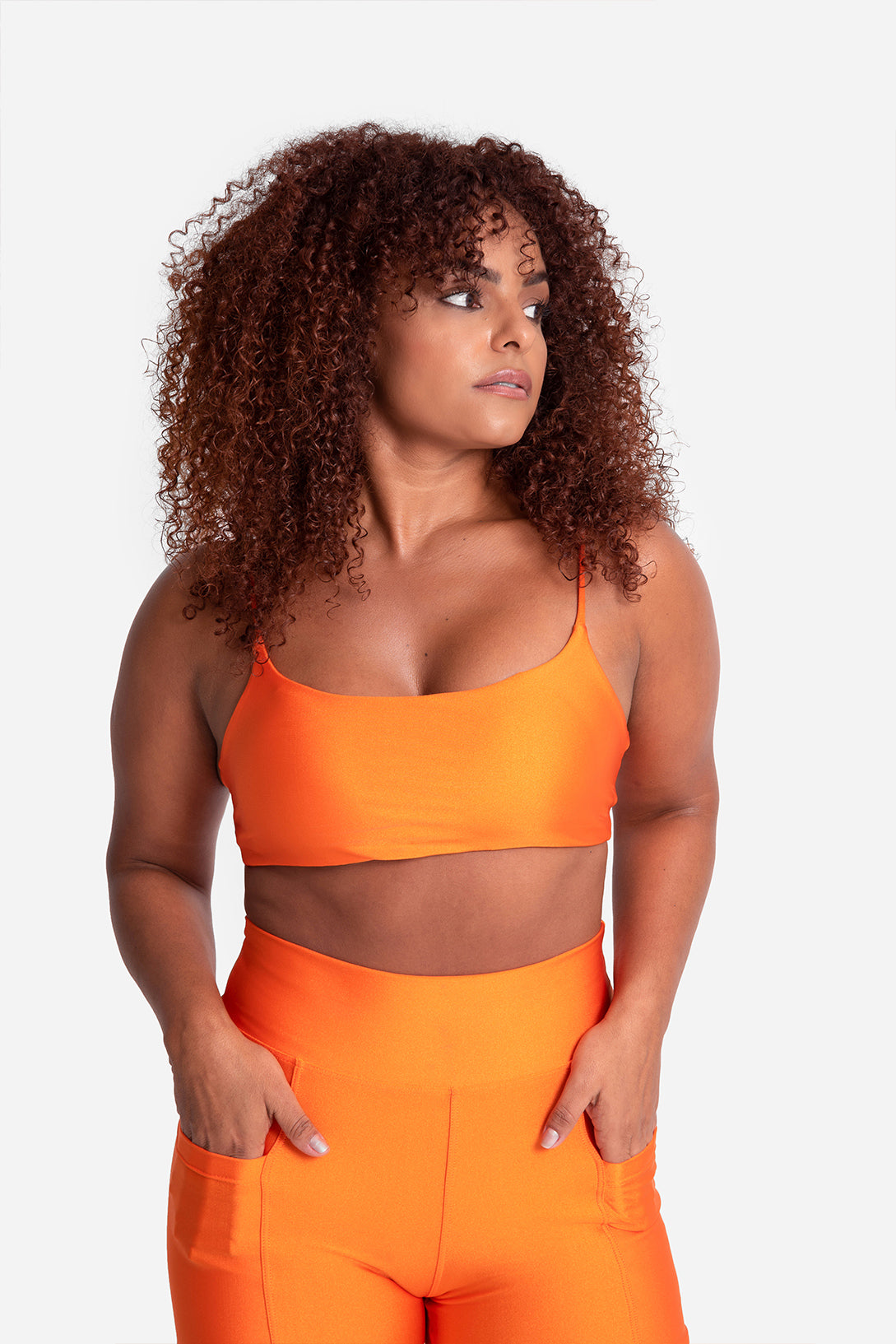Woman wearing an orange sports bra and leggings on a white background