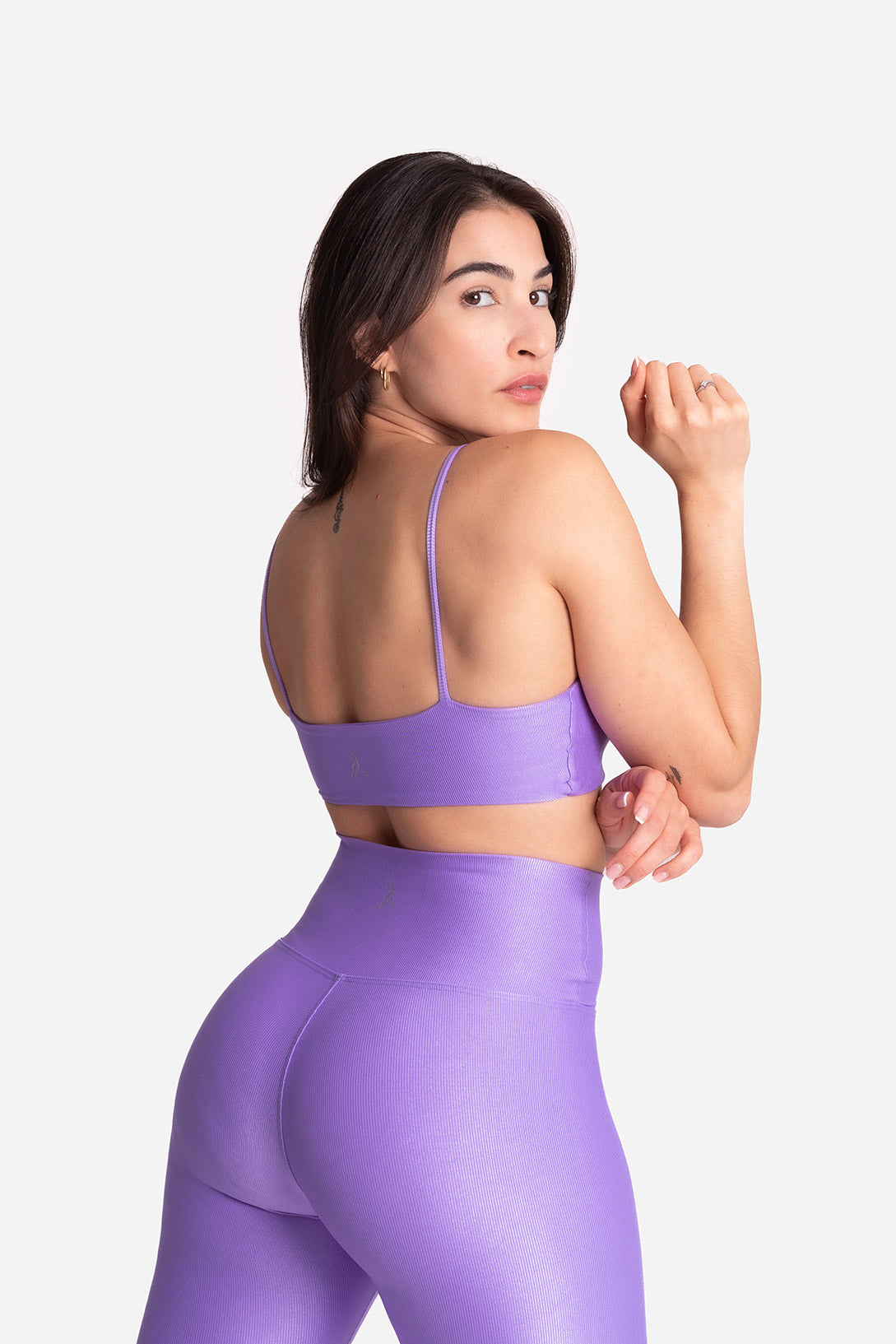 Woman wearing a purple sports bra and leggings on a light gray background