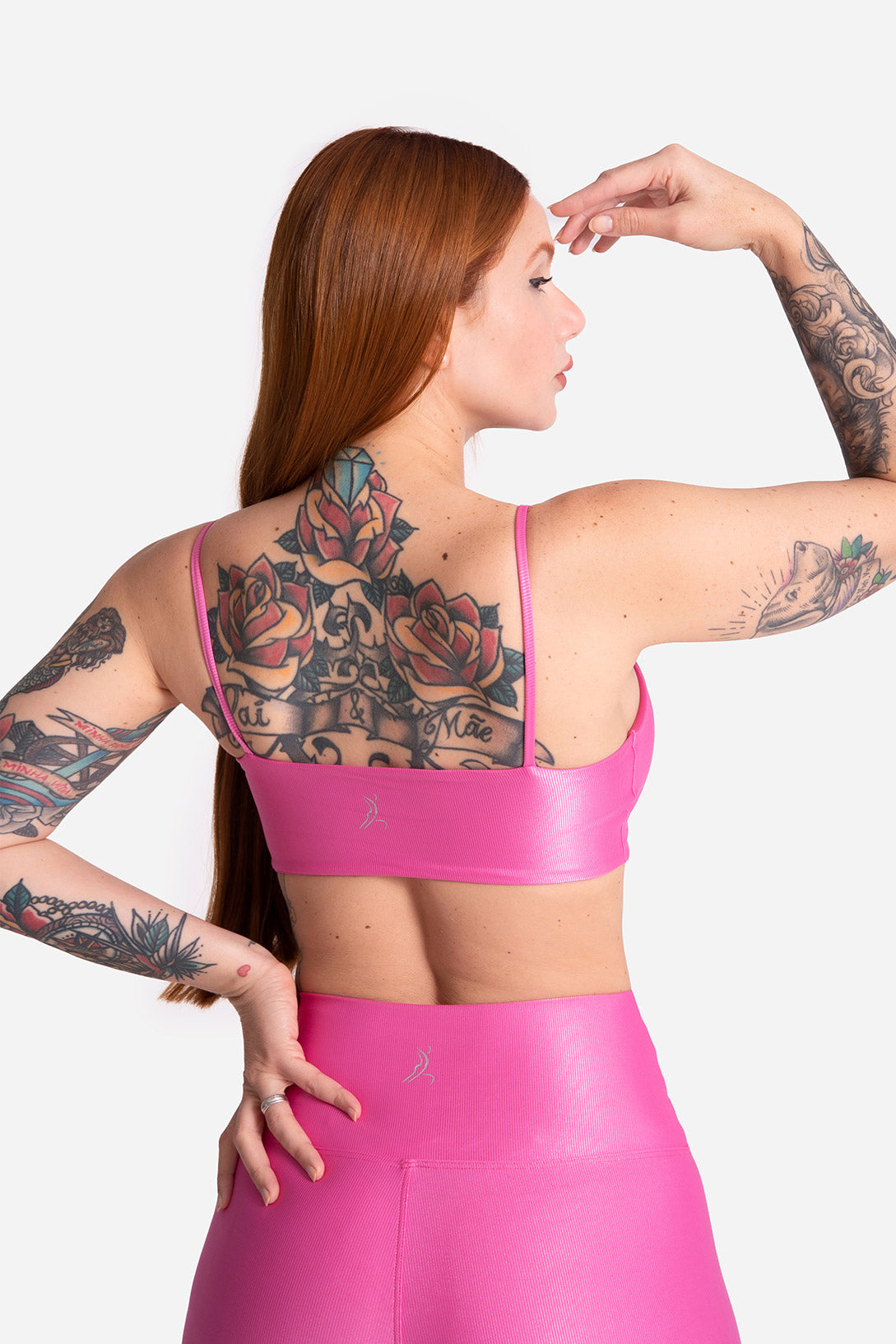 Woman wearing a pink sports bra and leggings with tattoos on a white background