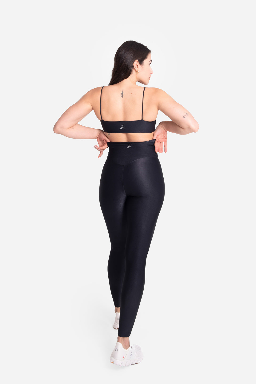 Woman wearing black athletic leggings and sports bra on a white background