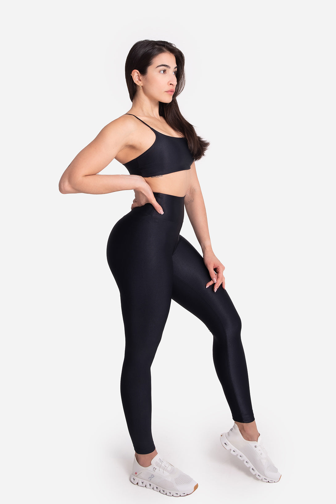 Woman wearing black athletic leggings and sports bra on a white background