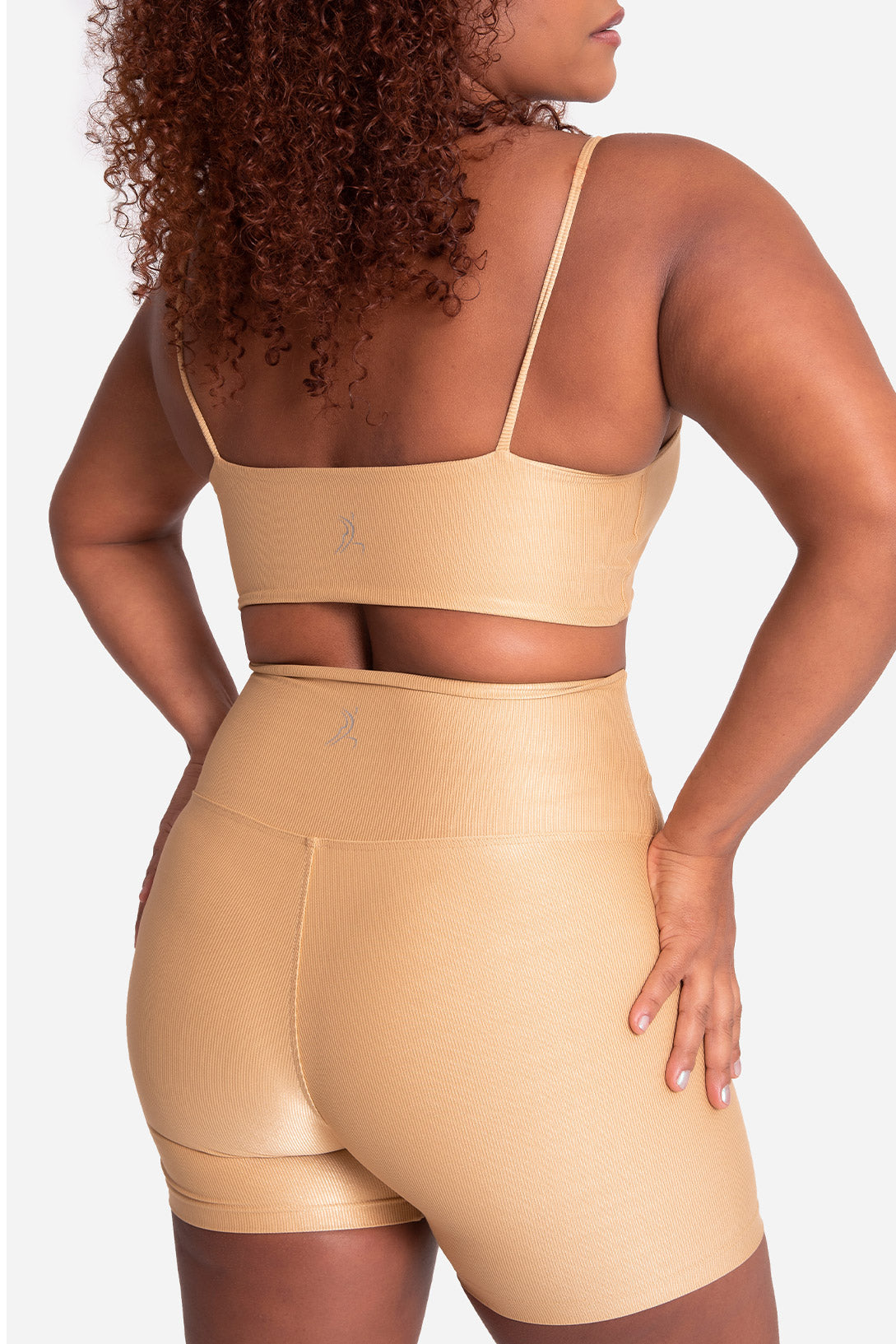 Person wearing a beige sports bra and shorts set on a white background
